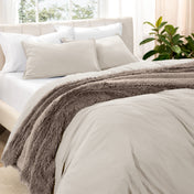 Washed bedding set on a bed in a bedroom with plants and nightstands.