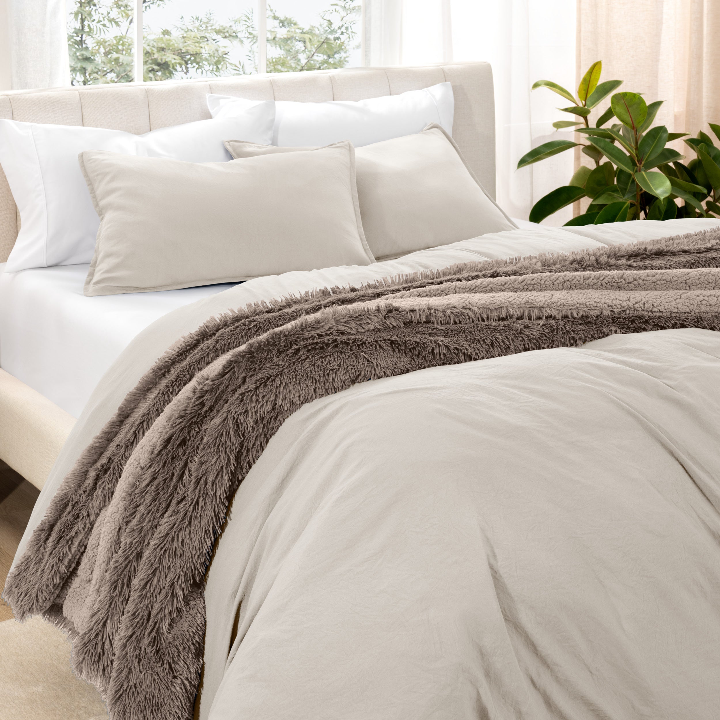 Washed bedding set on a bed in a bedroom with plants and nightstands.