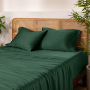 Bamboo bed sheets and pillows on a bed with a wicker headboard and plants in the background.
