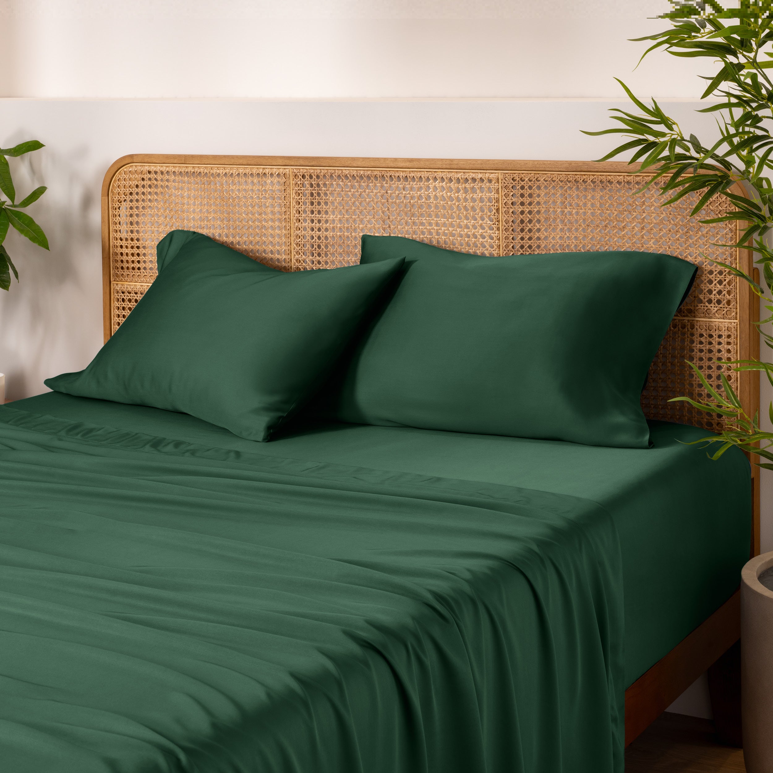 Bamboo bed sheets and pillows on a bed with a wicker headboard and plants in the background.