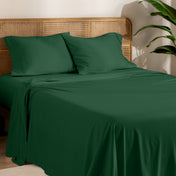 Organic cotton jersey bed sheets on a bed with a wicker headboard and plant in the background