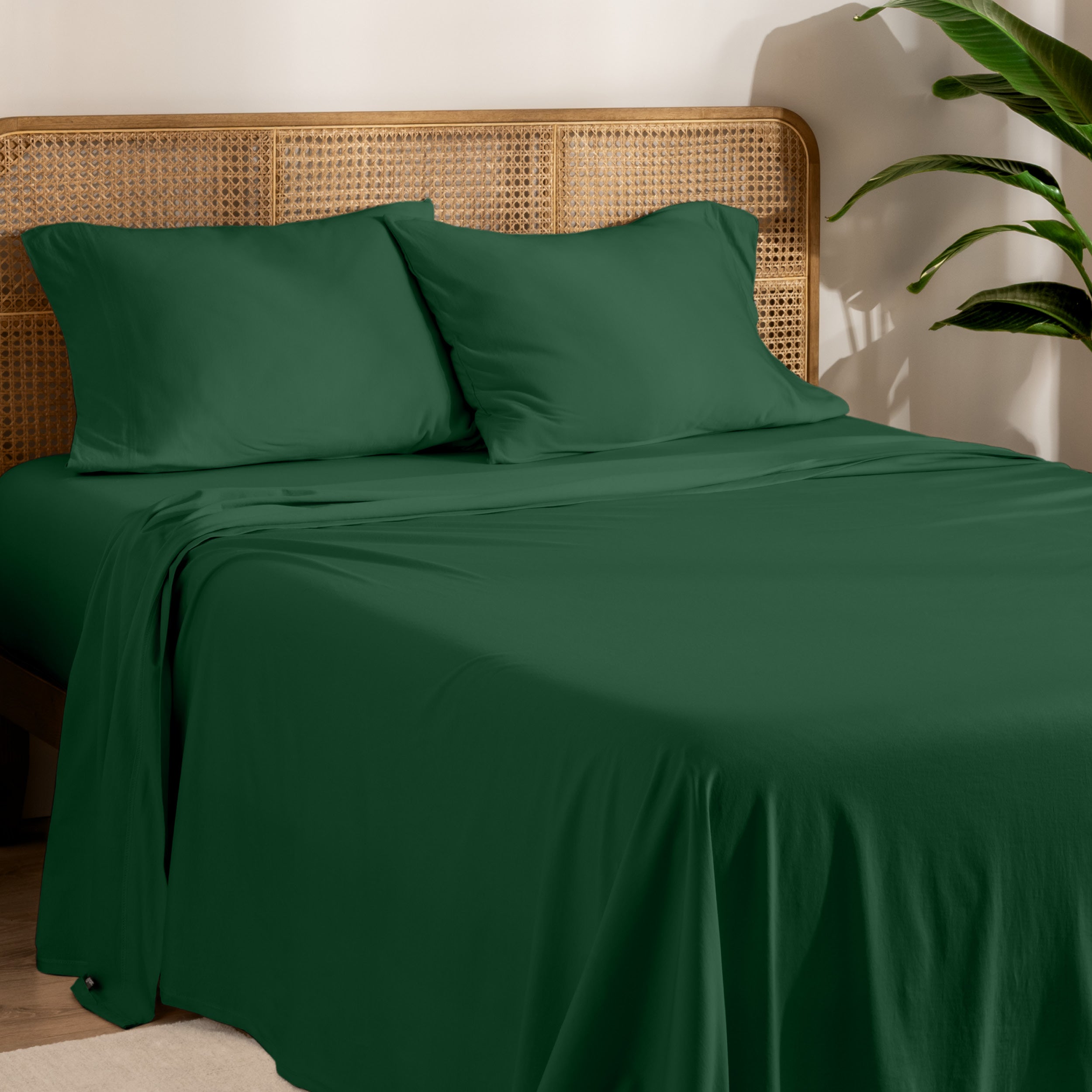 Organic cotton jersey bed sheets on a bed with a wicker headboard and plant in the background