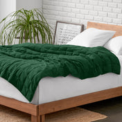 Weighted blanket on a bed with white pillows and a wooden headboard in a room with a plant and brick wall.