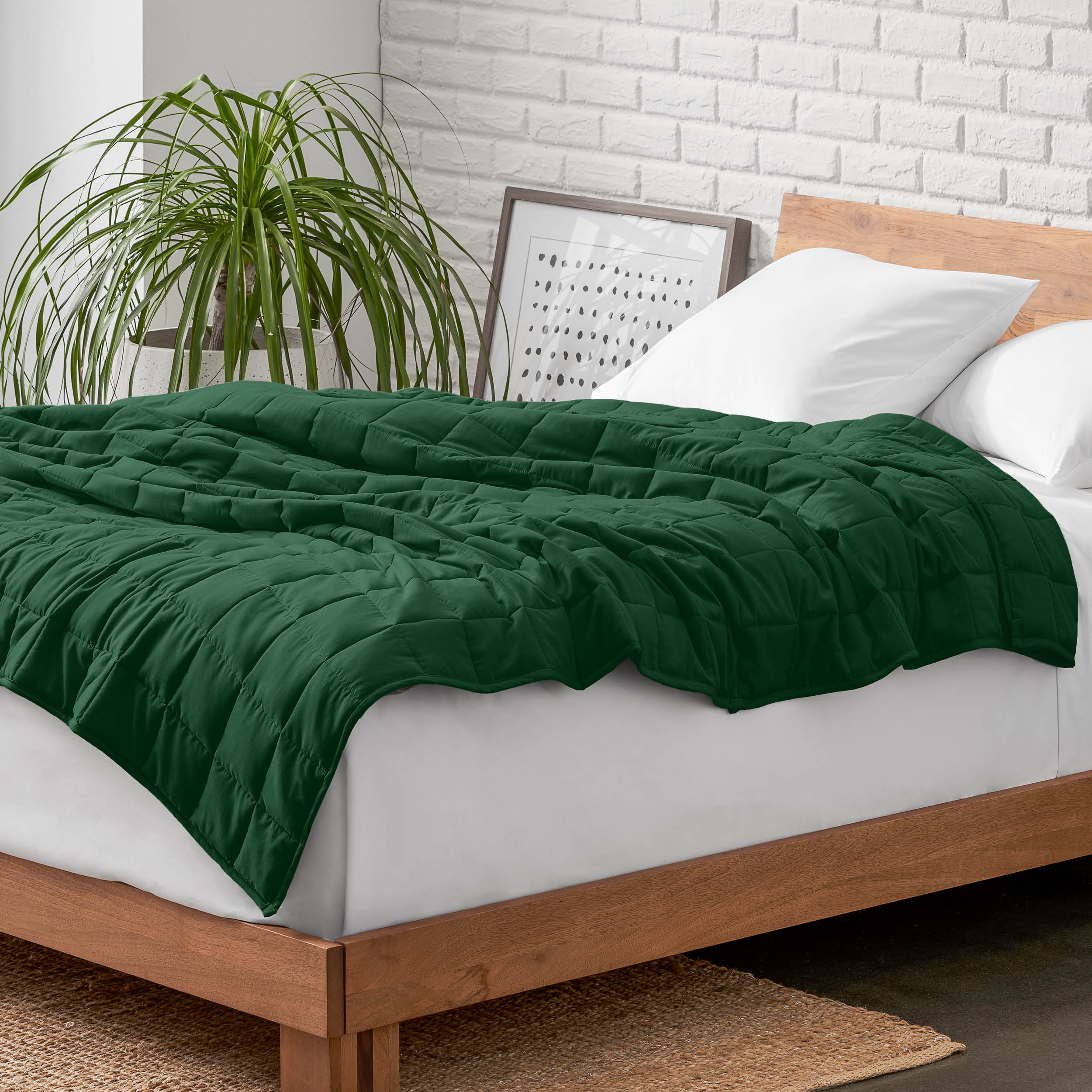 Weighted blanket on a bed with white pillows and a wooden headboard in a room with a plant and brick wall.