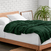 Weighted blanket on a bed with white pillows and a wooden headboard in a room with a plant and brick wall