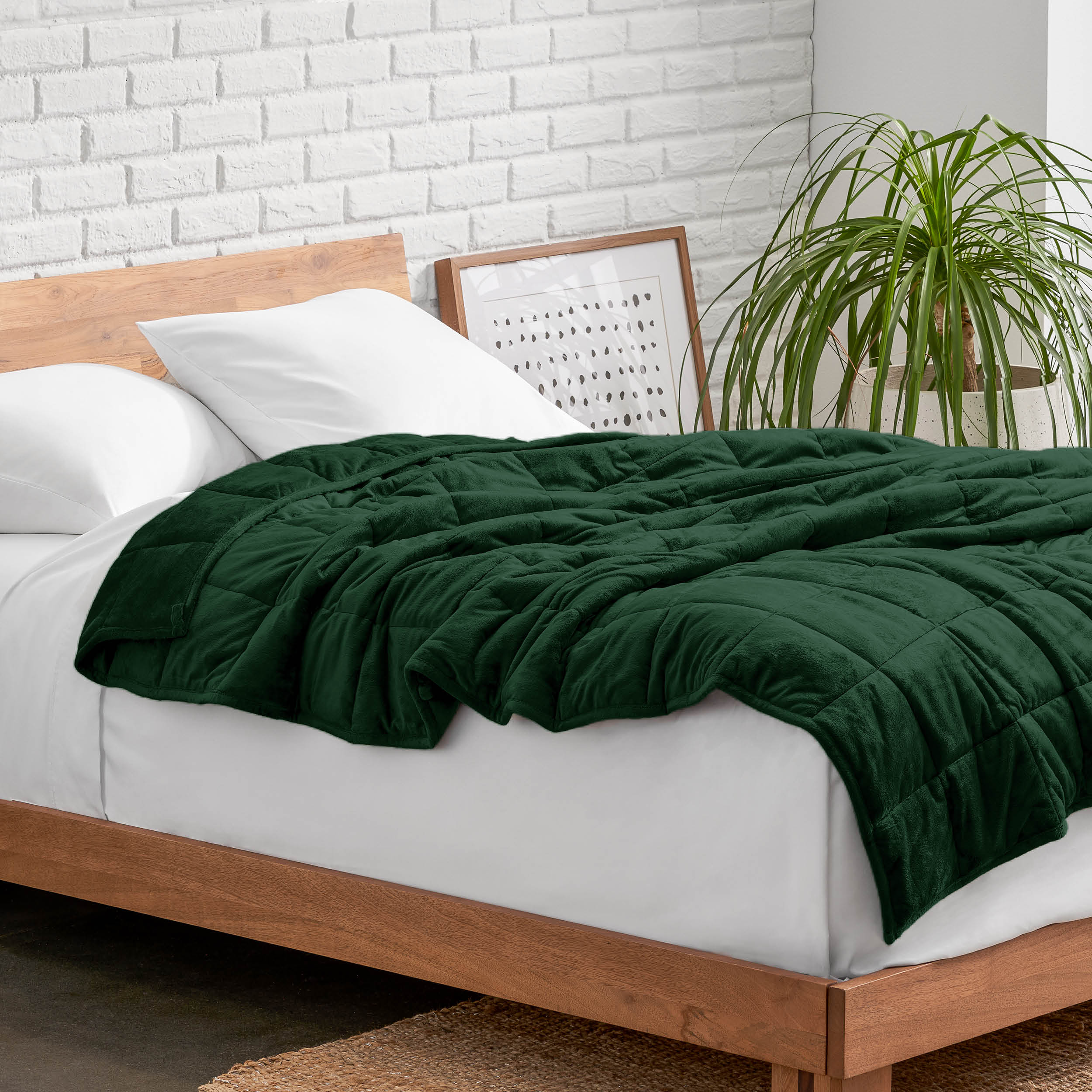 Weighted blanket on a bed with white pillows and a wooden headboard in a room with a plant and brick wall