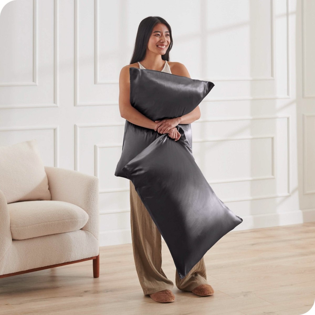 A woman standing while holding pillows with silk pillowcases on them