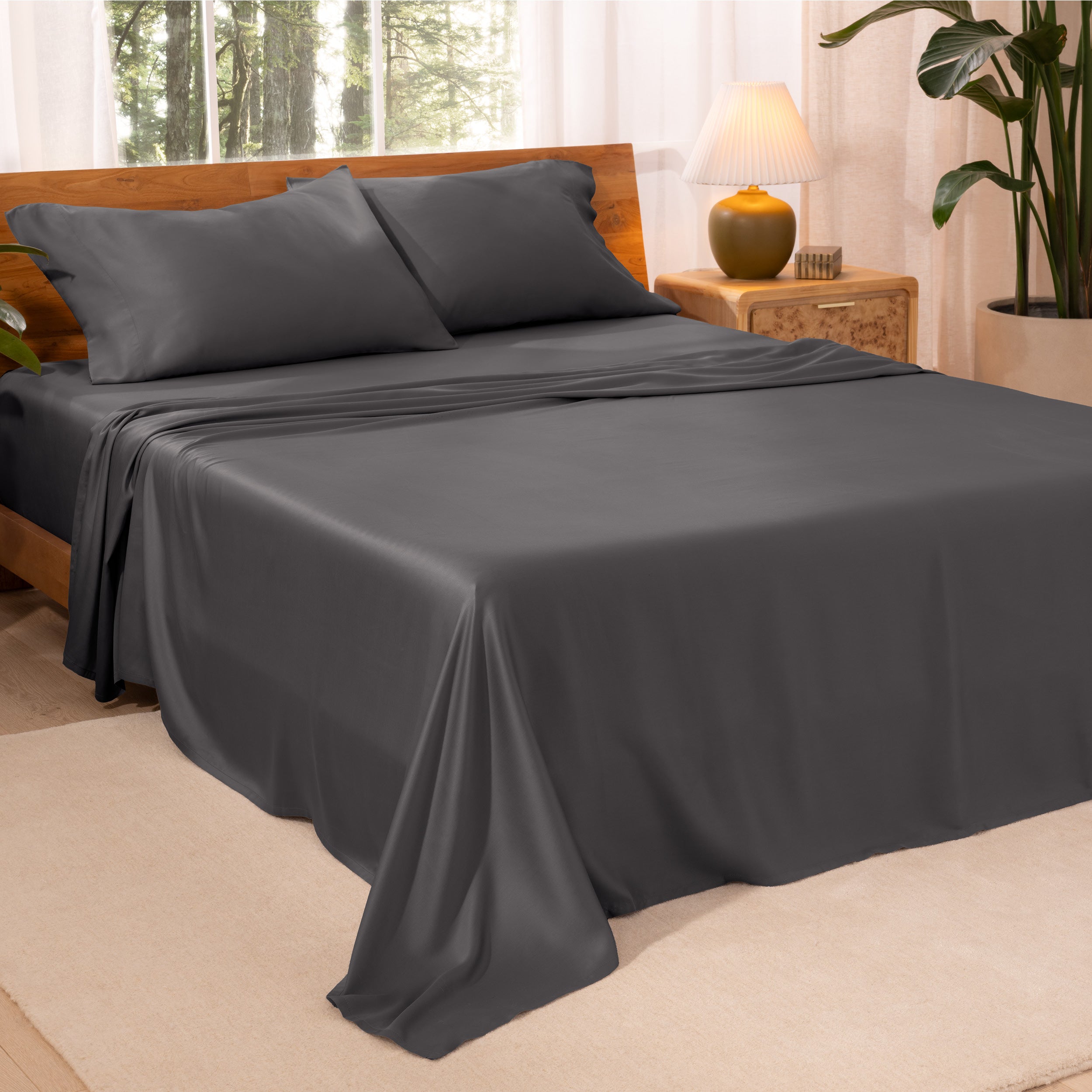 A bedroom with plants and a nightstand. Just sheets are on the bed.