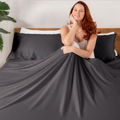 A smiling woman sitting on a bed with a flat sheet draped over her