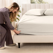 A woman is putting a fitted sateen sheet on a mattress