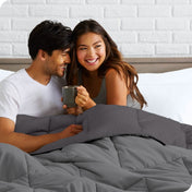 A couple sitting in bed with a reversible comforter over them