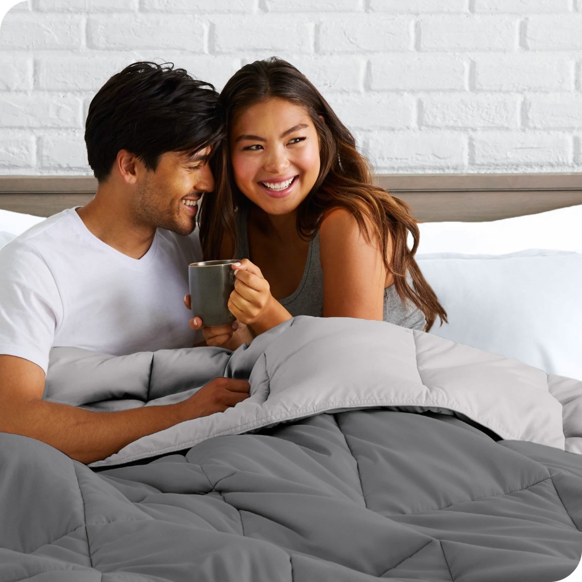 A couple sitting in bed with a reversible comforter over them