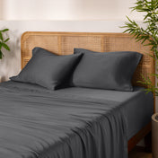 Bamboo bed sheets and pillows on a bed with a wicker headboard and plants in the background.