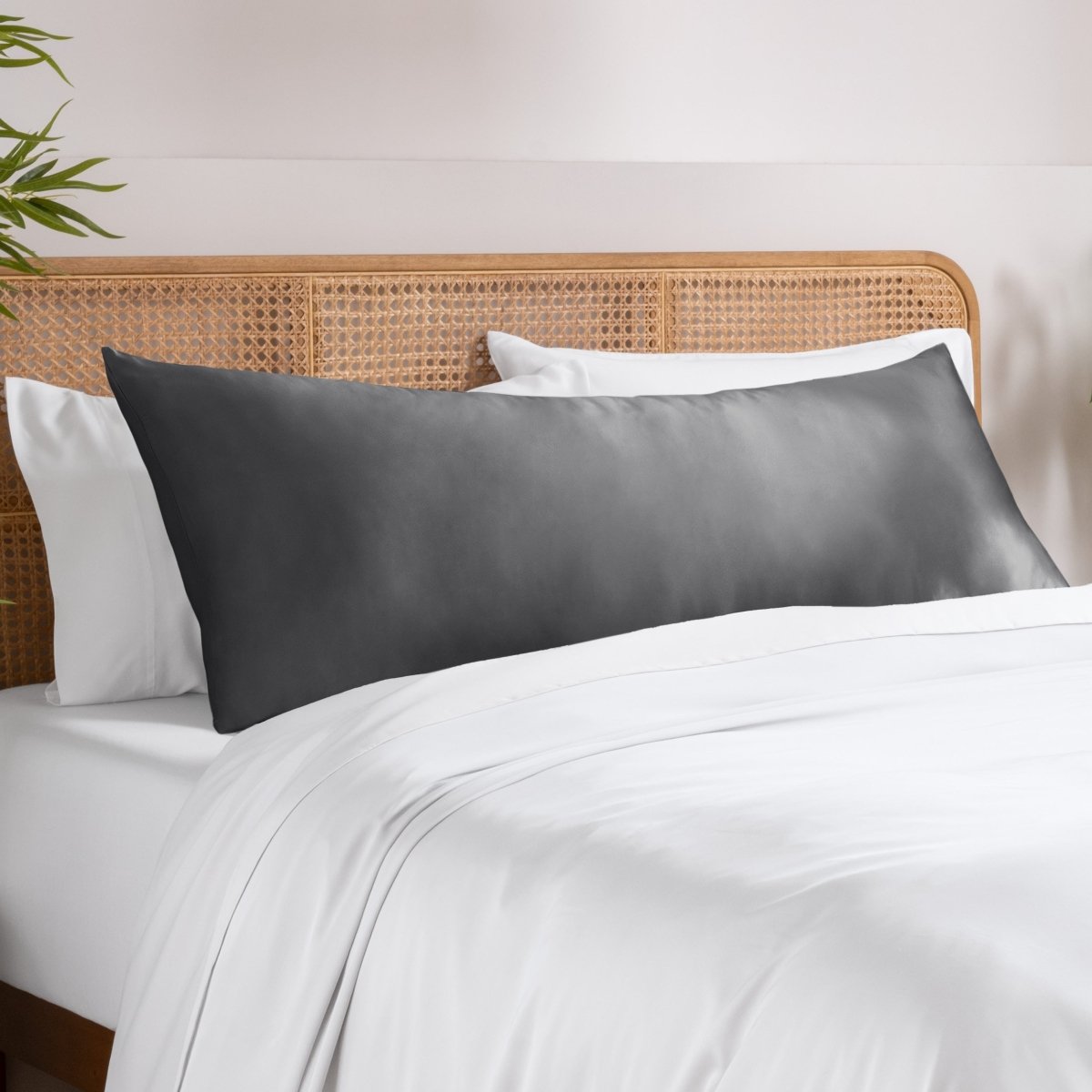 Body pillowcase on a pillow set on a bed with a wicker headboard and a plant in the corner.