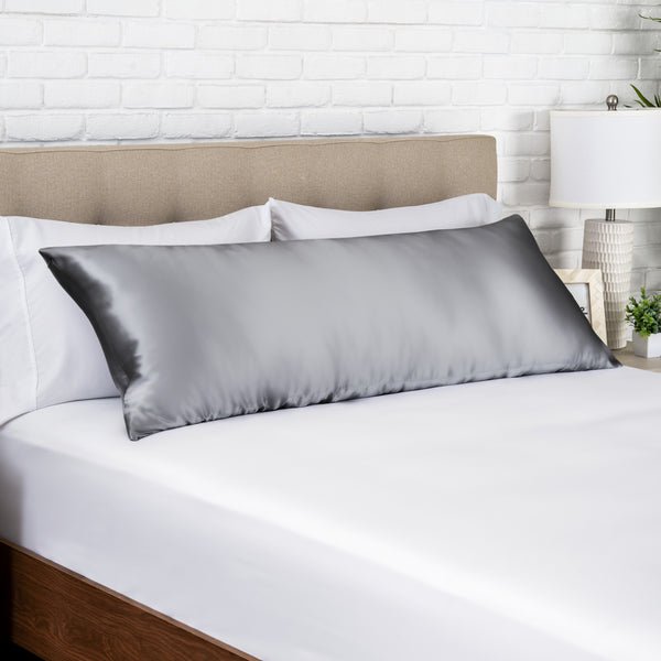 Gray silk pillow on a bed with white bedding and a beige headboard.