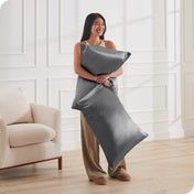 A woman is standing and holding 2 pillows covered with silk pillowcases