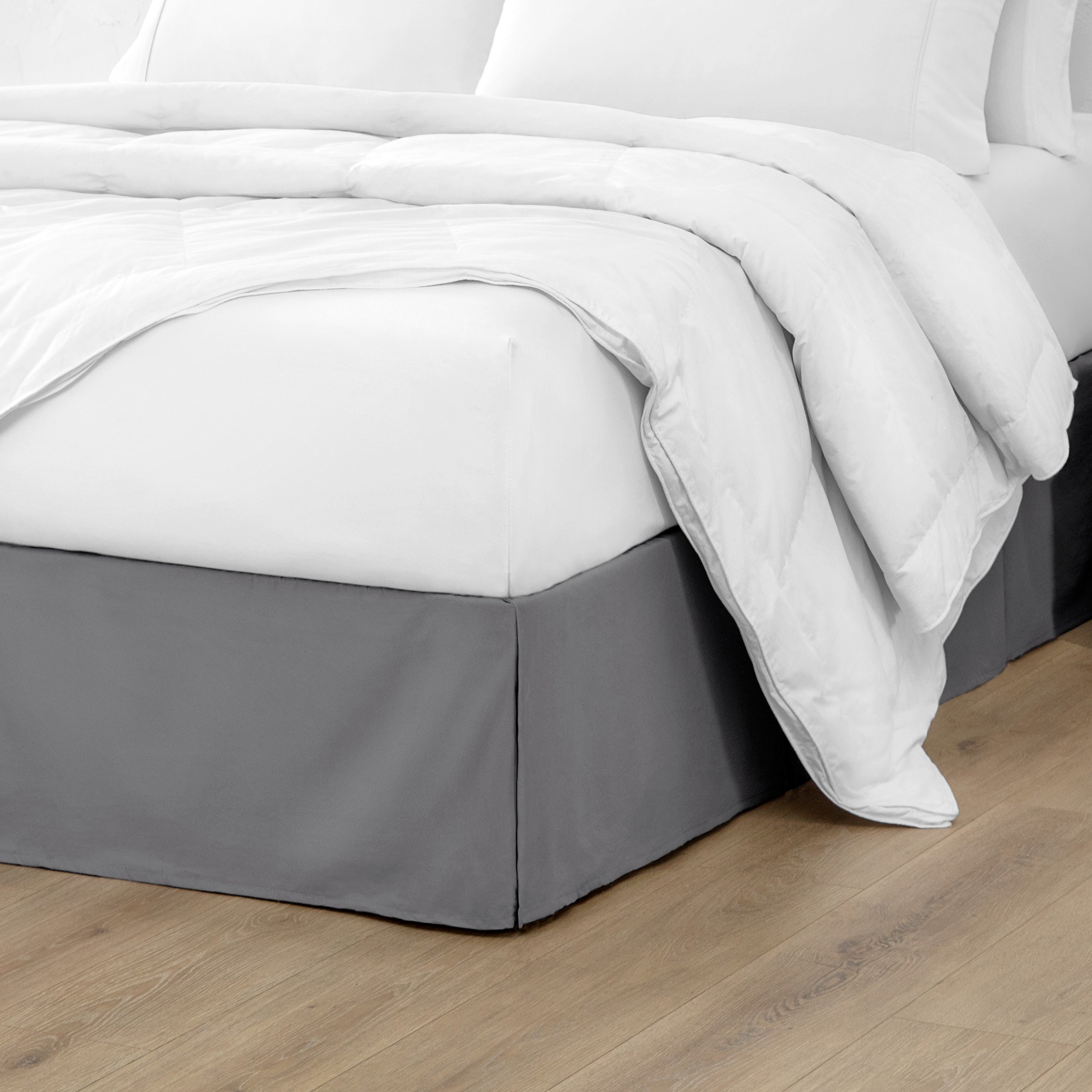 A modern bed with a microfiber bed skirt with pleats on the corners and midway on each side