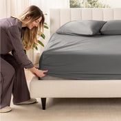 A woman is putting a fitted sateen sheet on a mattress