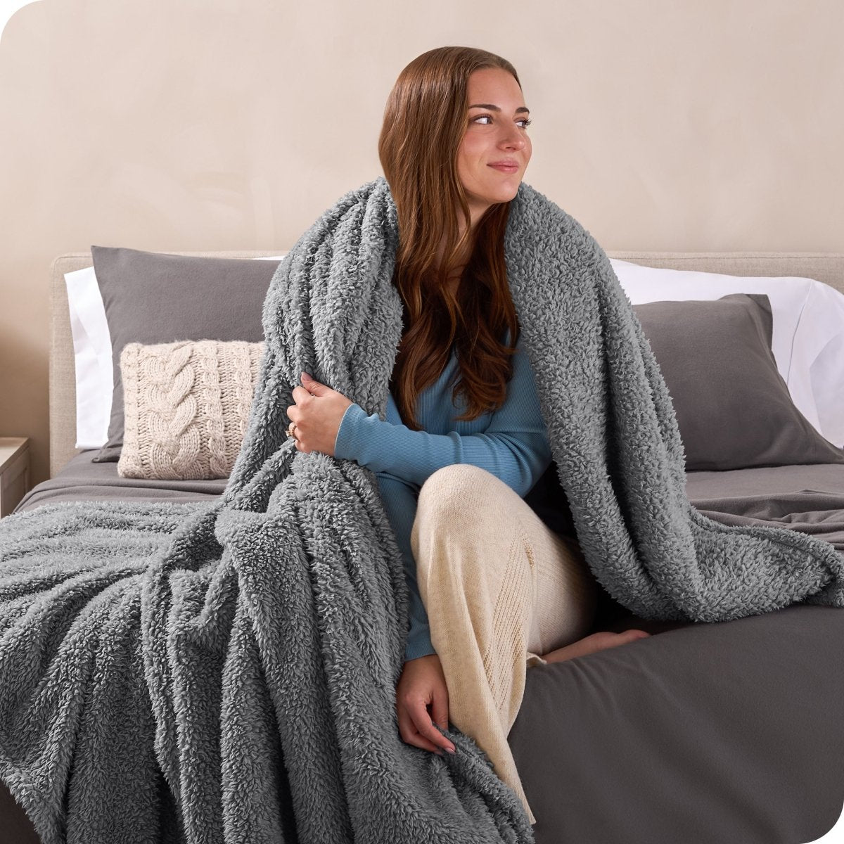 A woman sitting on a bed wrapped in a sherpa blanket