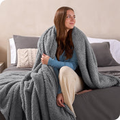 A woman sitting on a bed wrapped in a sherpa blanket