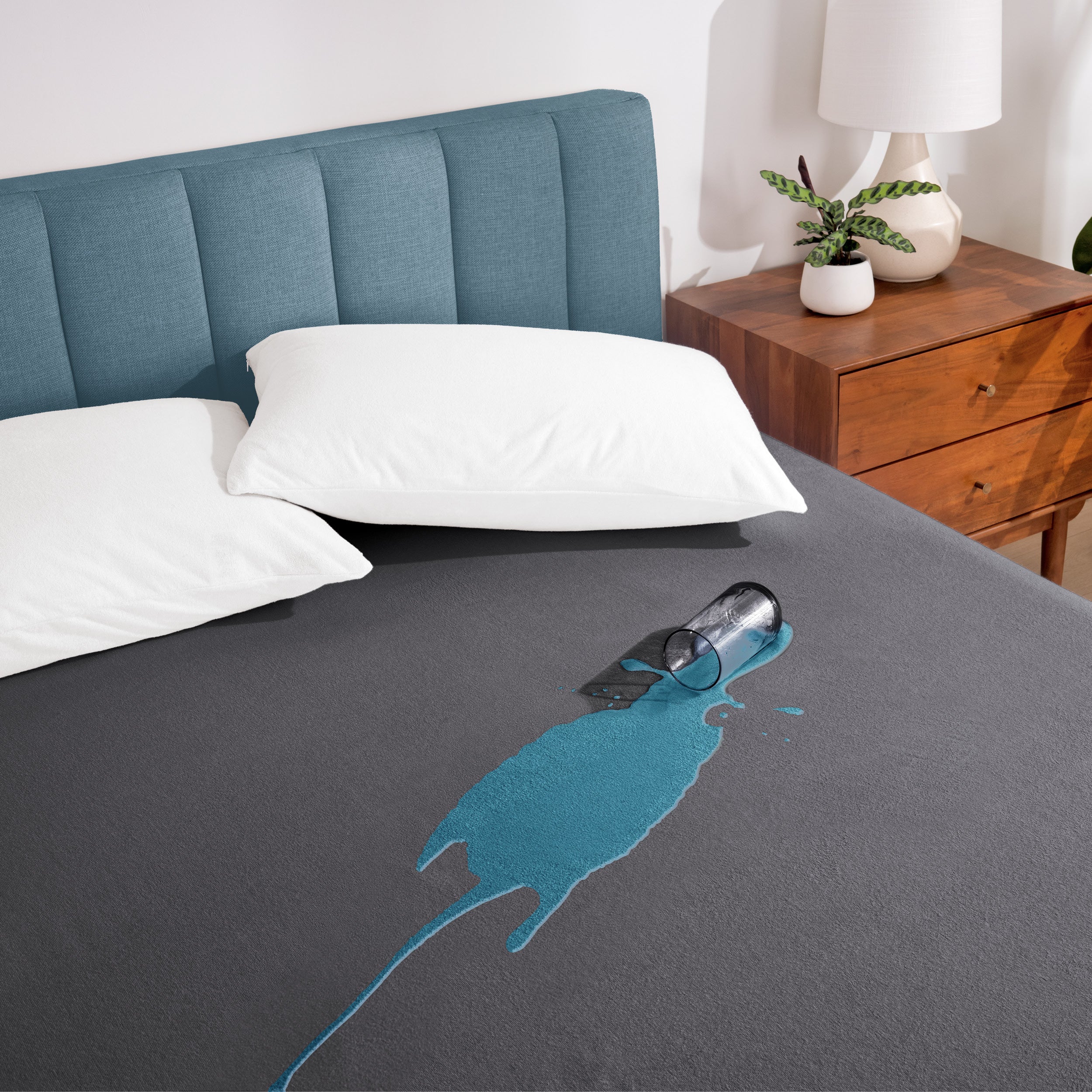 A glass of water spilled on a bed covered with a mattress protector