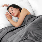 Woman sleeping peacefully under a weighted blanket with white pillows
