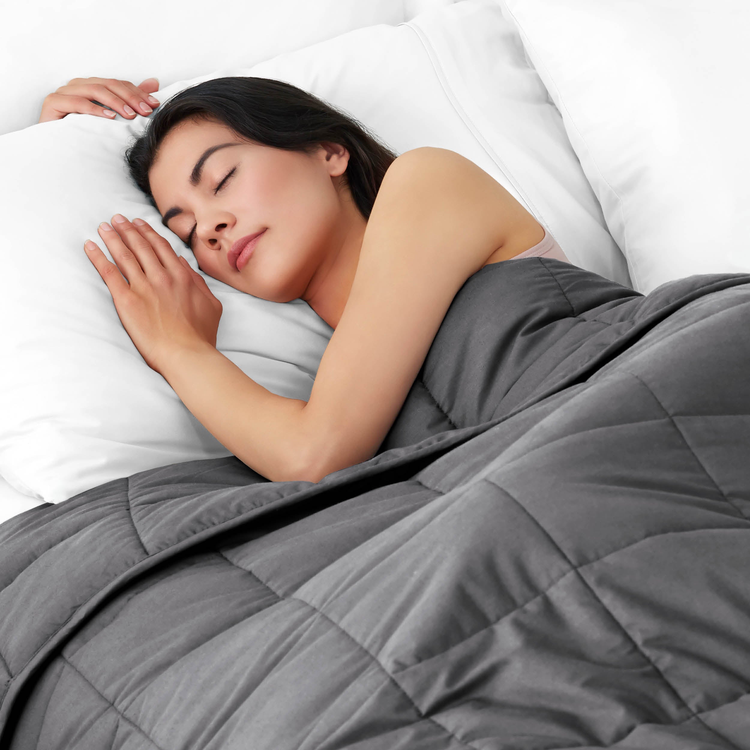 Woman sleeping peacefully under a weighted blanket with white pillows
