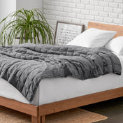 Weighted blanket on a bed with white pillows and a wooden headboard in a room with a plant and brick wall.