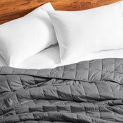Cotton weighted blanket on a bed with white pillows against a wooden headboard.