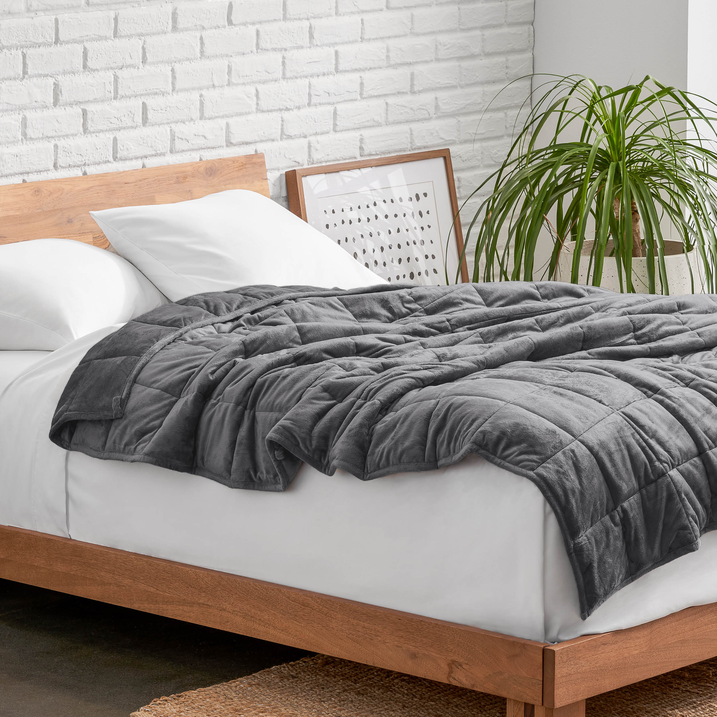 Weighted blanket on a bed with white pillows and a wooden headboard in a room with a plant and brick wall