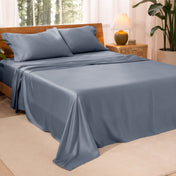 A bedroom with plants and a nightstand. Just sheets are on the bed.