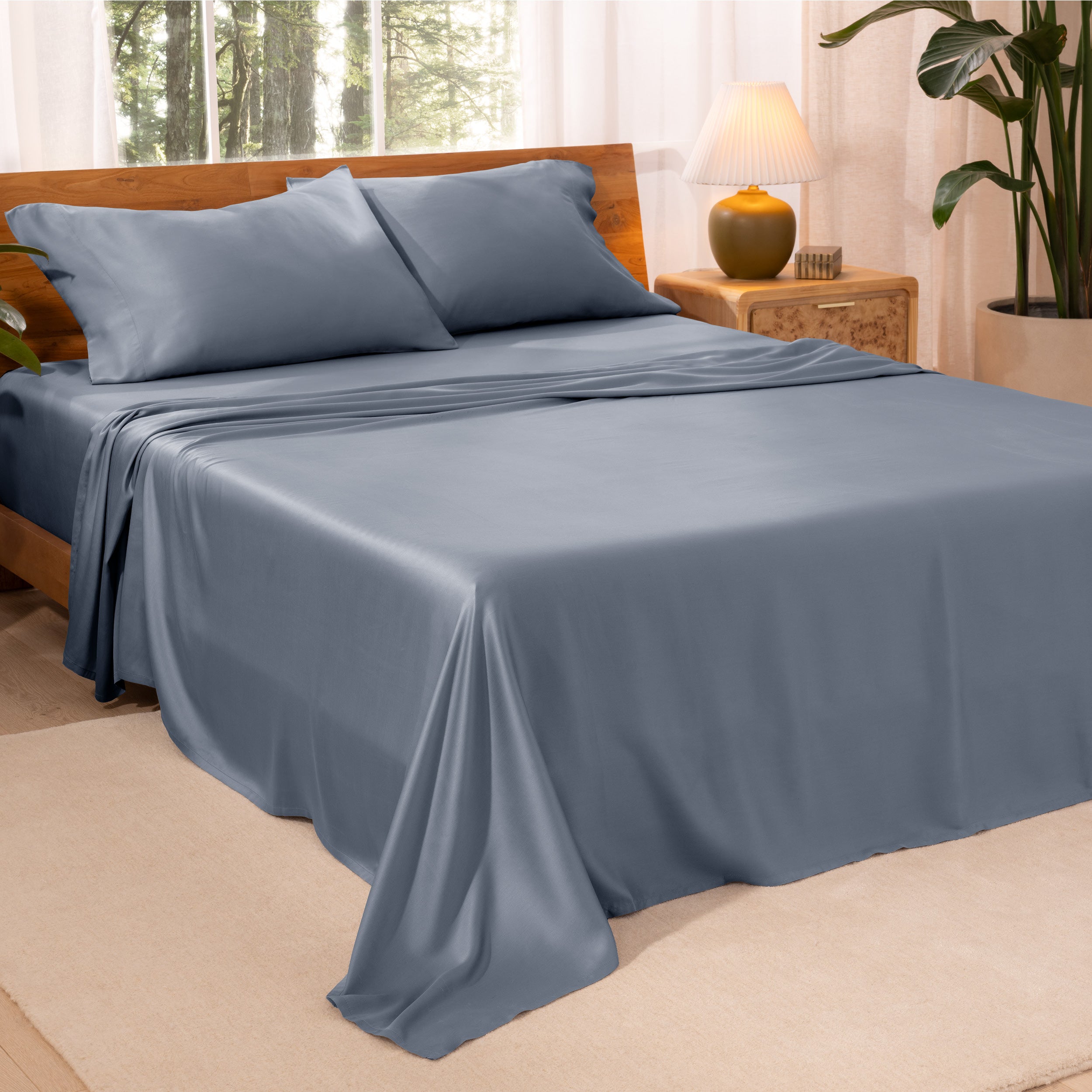 A bedroom with plants and a nightstand. Just sheets are on the bed.