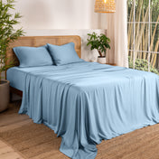 Bamboo sheets on a bed in a bedroom with plants and a lamp.
