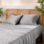 Bamboo bed sheets and pillows on a bed with a wicker headboard and plants in the background.