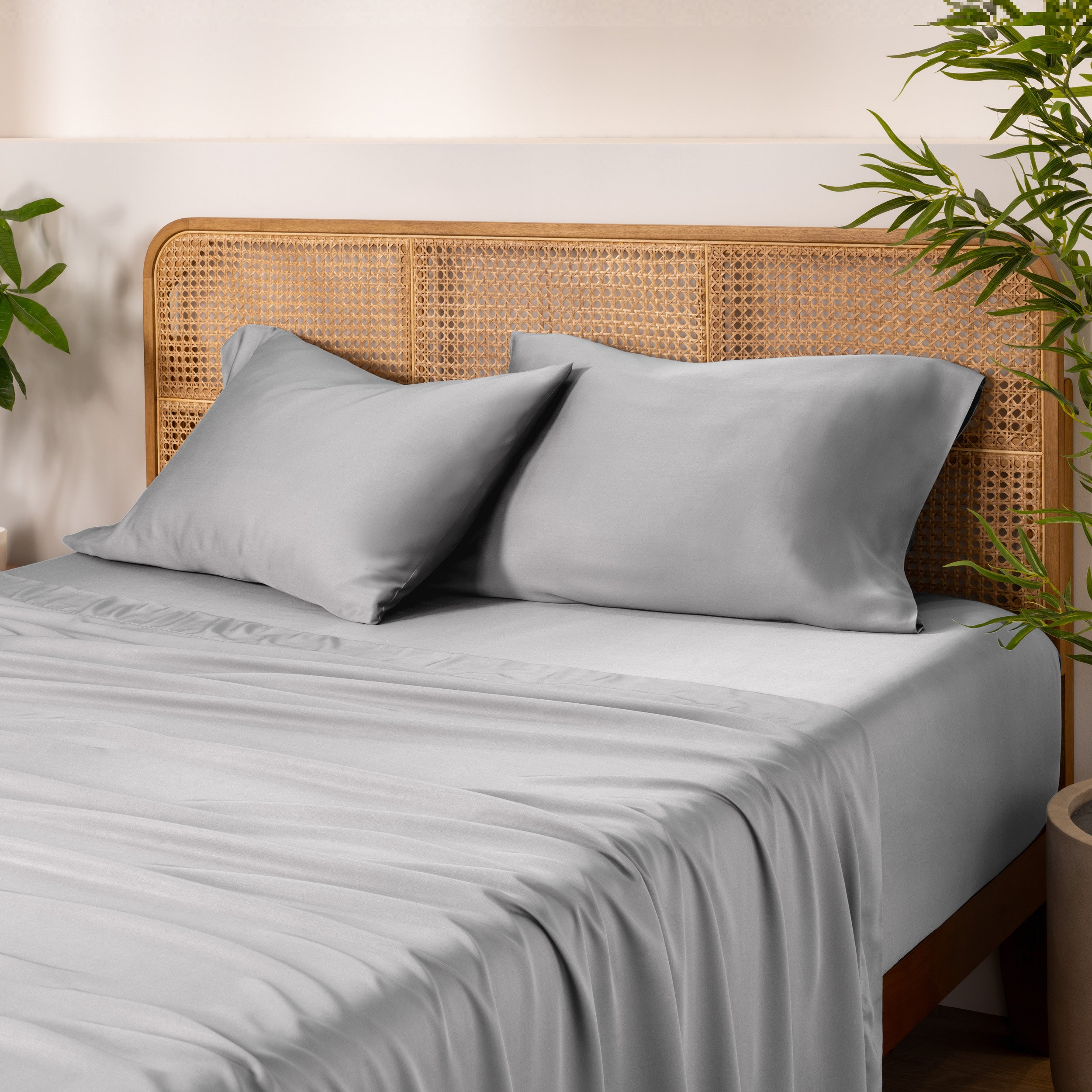 Bamboo bed sheets and pillows on a bed with a wicker headboard and plants in the background.