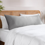 Body pillowcase on a pillow set on a bed with a wicker headboard and a plant in the corner.