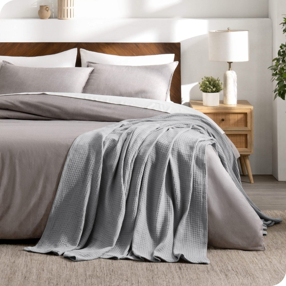 A cotton waffle blanket is on the corner of a bed. It is hanging down the side and end of the bed.
