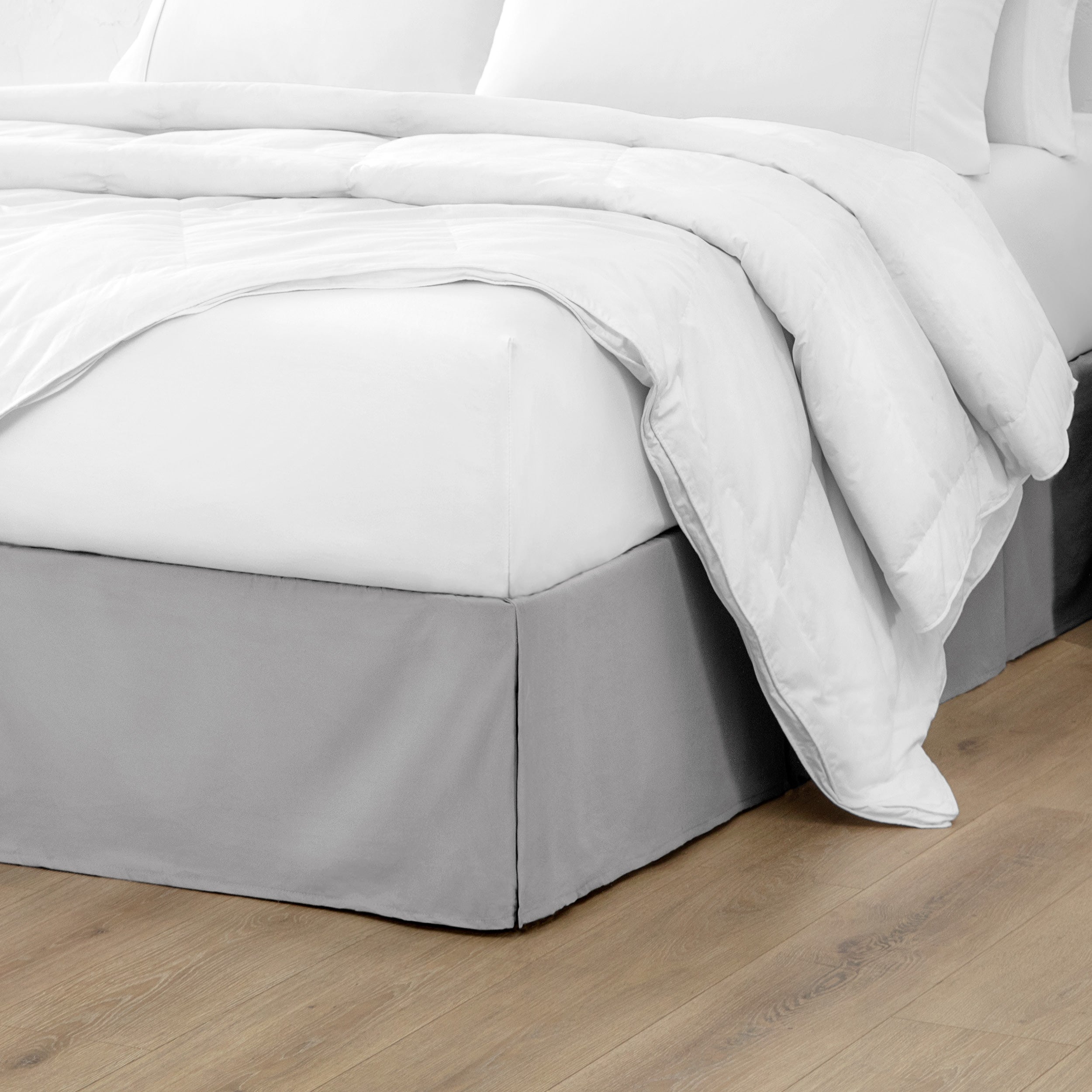 A modern bed with a microfiber bed skirt with pleats on the corners and midway on each side