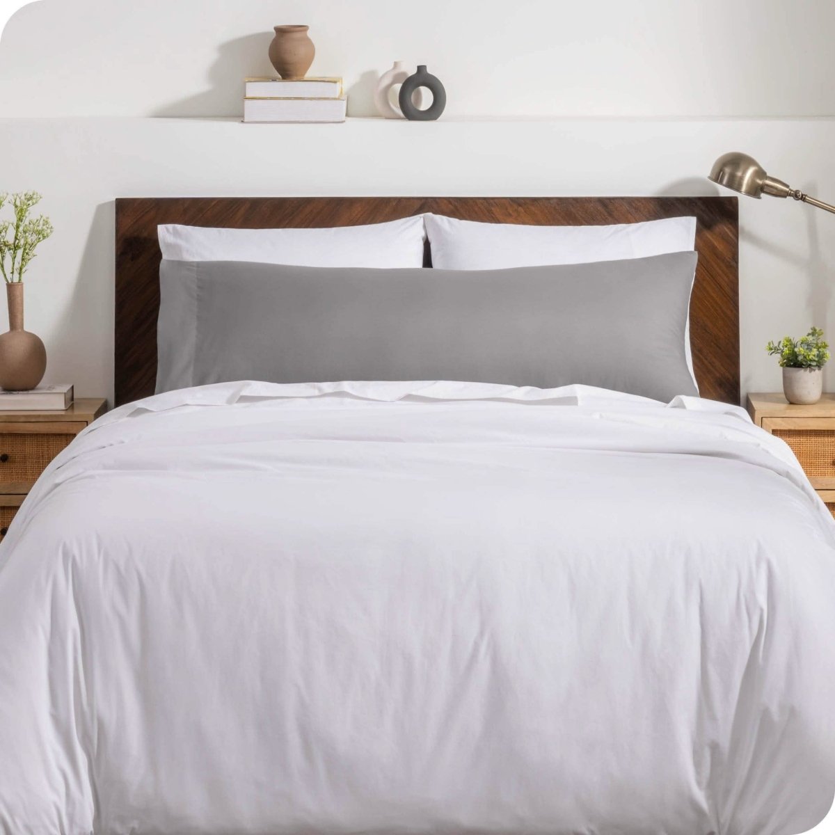 A body pillow cover on a pillow on a bed with other pillows and a duvet cover