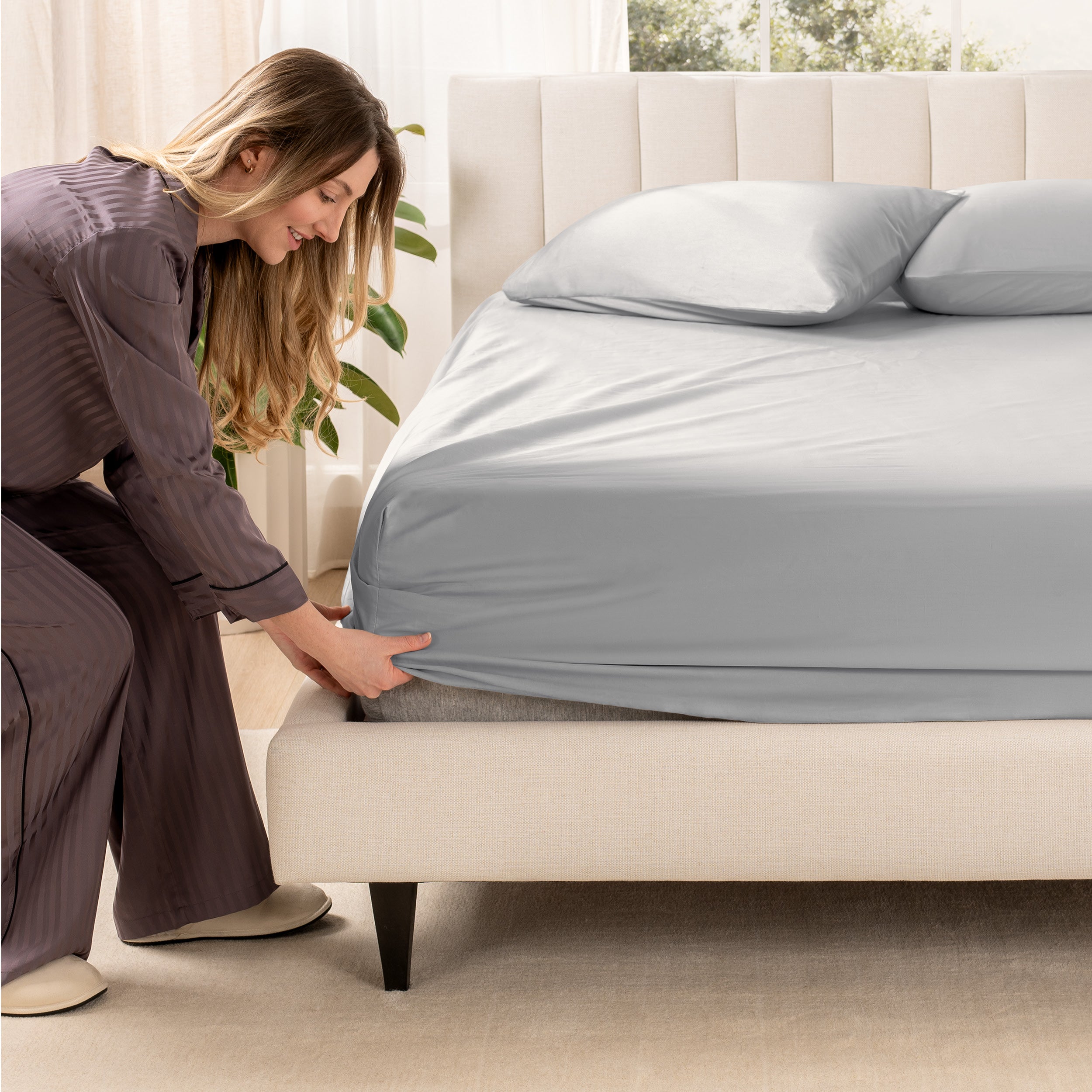 A woman is putting a fitted sateen sheet on a mattress