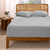 Bed with fitted sheet and pillows in a room with curtains and a plant.