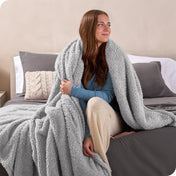 A woman sitting on a bed wrapped in a sherpa blanket