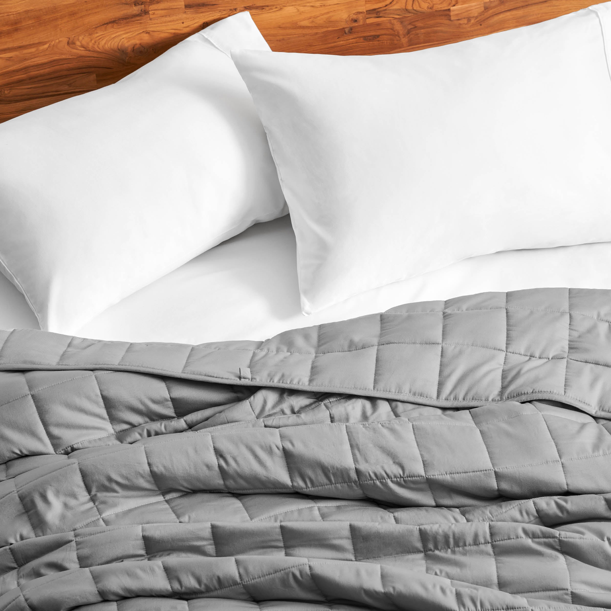 Cotton weighted blanket on a bed with white pillows against a wooden headboard.