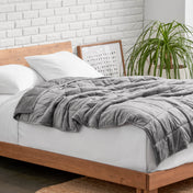 Weighted blanket on a bed with white pillows and a wooden headboard in a room with a plant and brick wall