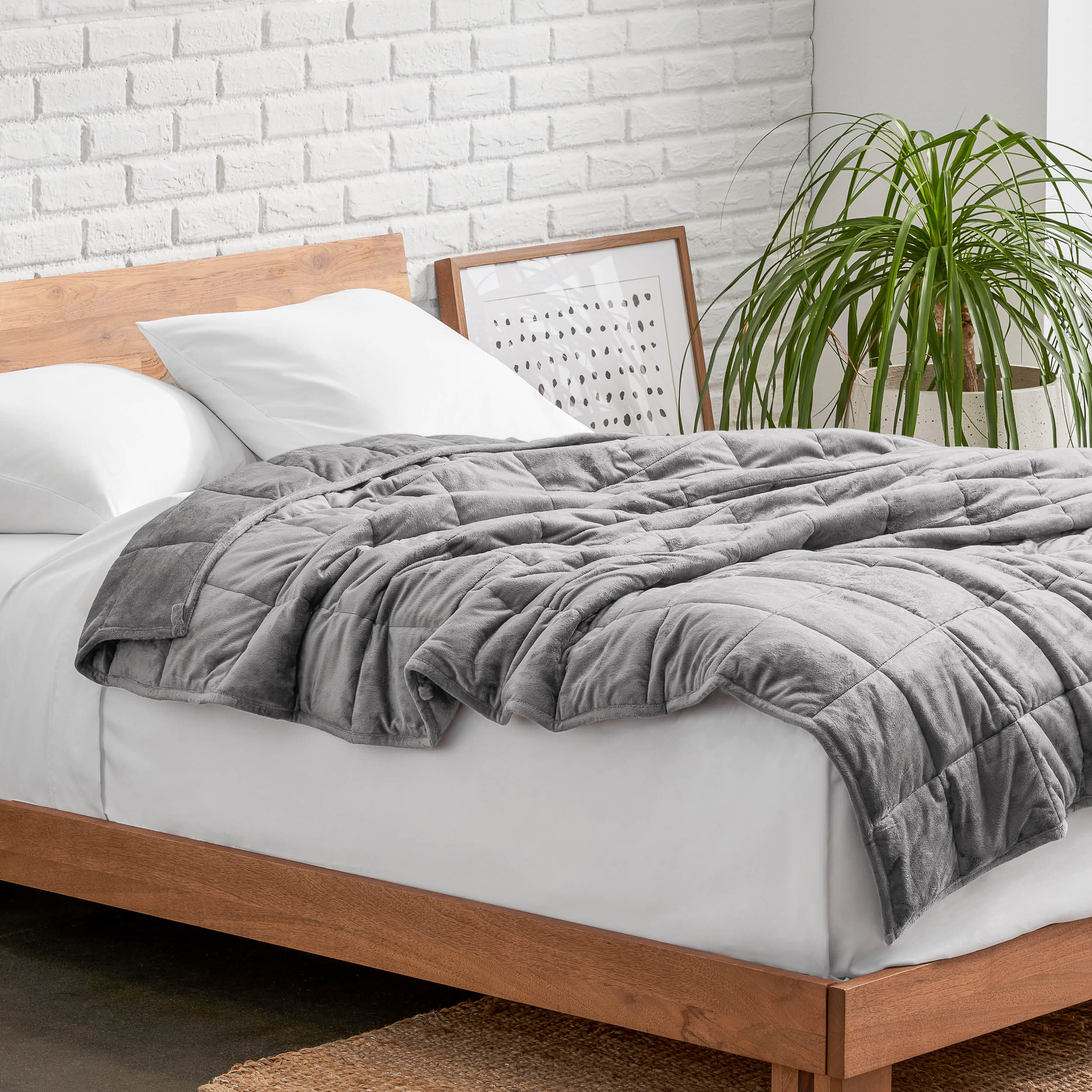 Weighted blanket on a bed with white pillows and a wooden headboard in a room with a plant and brick wall