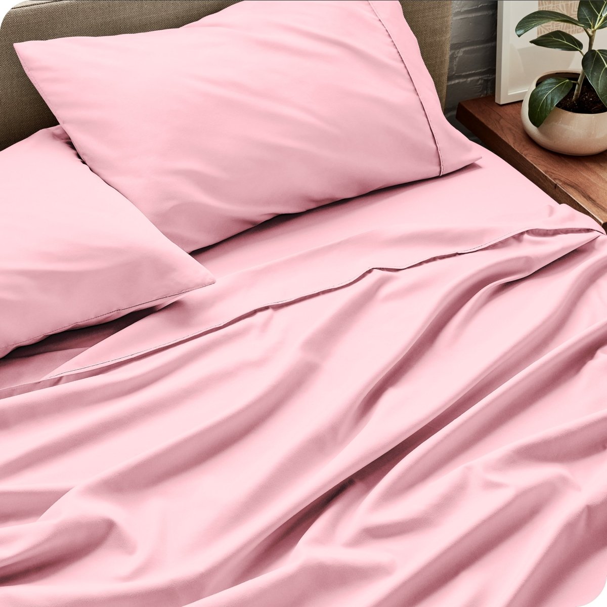 Bed sheets and pillows on a bed with a plant in the background