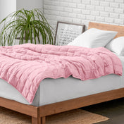 Weighted blanket on a bed with white pillows and a wooden headboard in a room with a plant and brick wall.