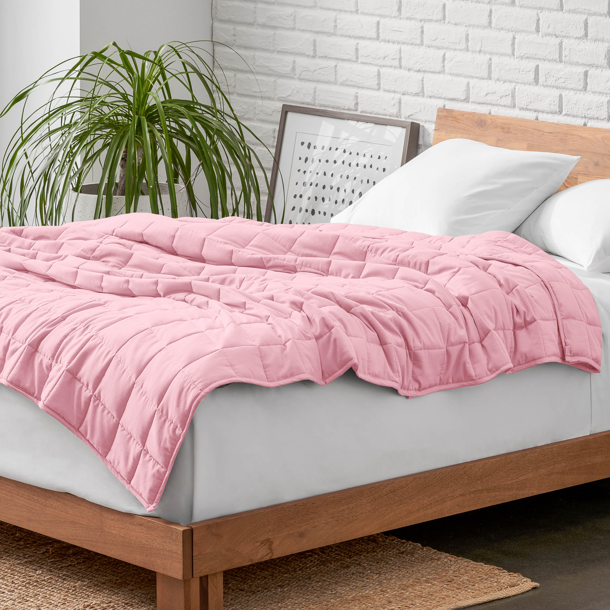 Weighted blanket on a bed with white pillows and a wooden headboard in a room with a plant and brick wall.