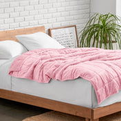 Weighted blanket on a bed with white pillows and a wooden headboard in a room with a plant and brick wall