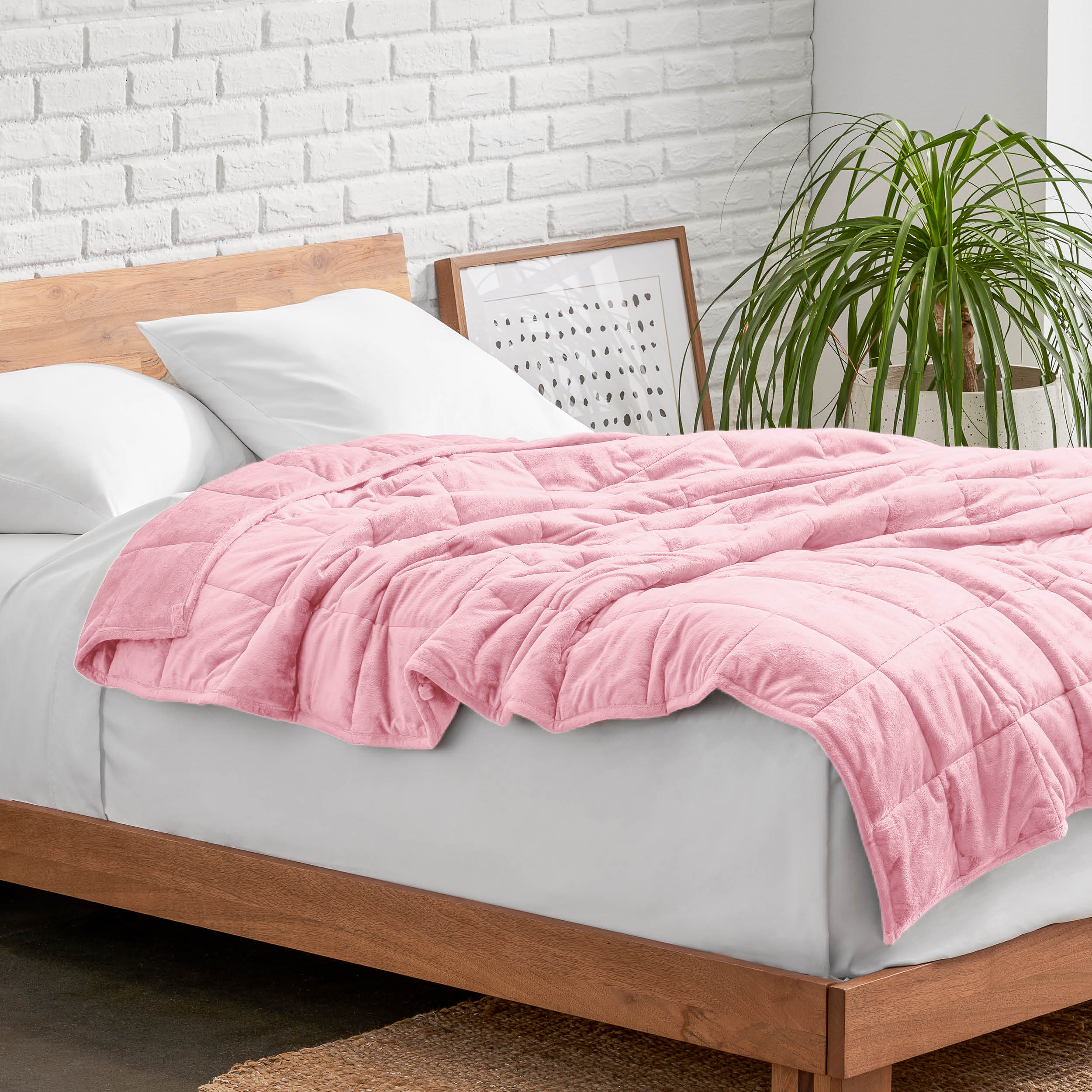 Weighted blanket on a bed with white pillows and a wooden headboard in a room with a plant and brick wall